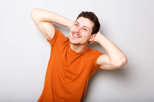 Portret van gelukkige jonge man die lacht met handen achter hoofd tegen de grijze achtergrond - Foto, afbeelding