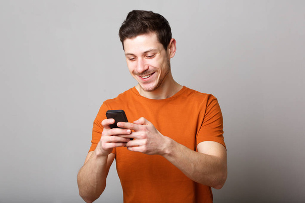 Портрет улыбающегося молодого человека, смотрящего на текстовое сообщение на мобильном телефоне
 - Фото, изображение