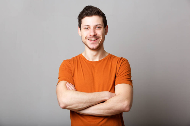 Портрет уверенного молодого человека, стоящего со скрещенными руками на сером фоне
 - Фото, изображение