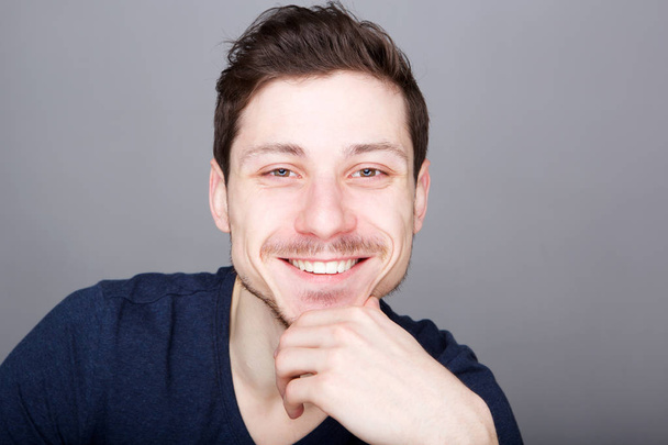 Detailní záběr portrét pohledný mladý muž s úsměvem s rukou na bradě  - Fotografie, Obrázek