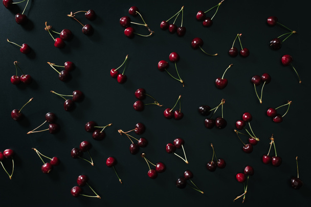 top view of fresh ripe red sweet cherries on black background - Foto, afbeelding
