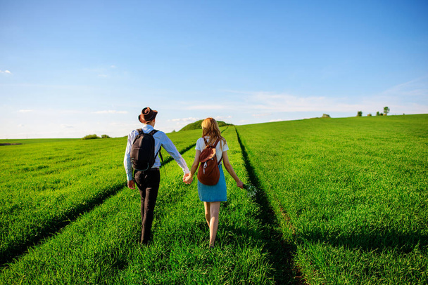 Con una mochila, un hombre con sombrero y una mujer con el pelo largo van por el camino. Una pareja camina por el prado
. - Foto, imagen