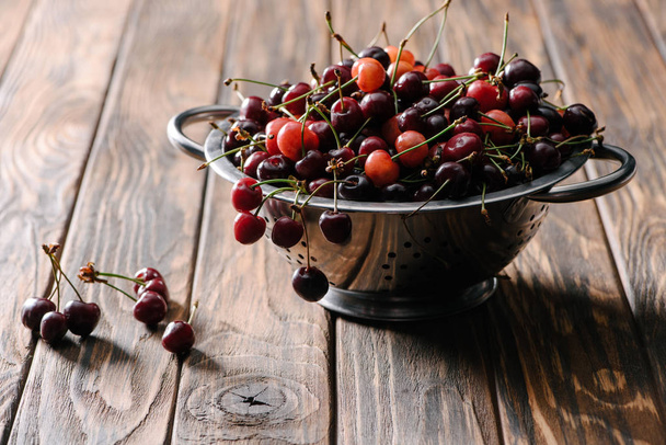 colander with fresh sweet healthy cherries on rustic wooden table - Foto, afbeelding
