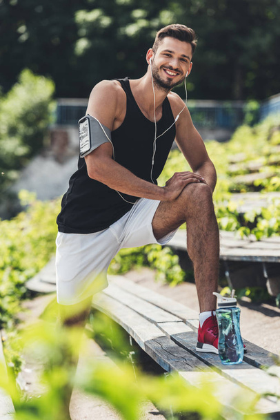 sportif heureux dans les écouteurs avec smartphone dans le boîtier du brassard de course faire de l'exercice sur le banc au terrain de sport
 - Photo, image