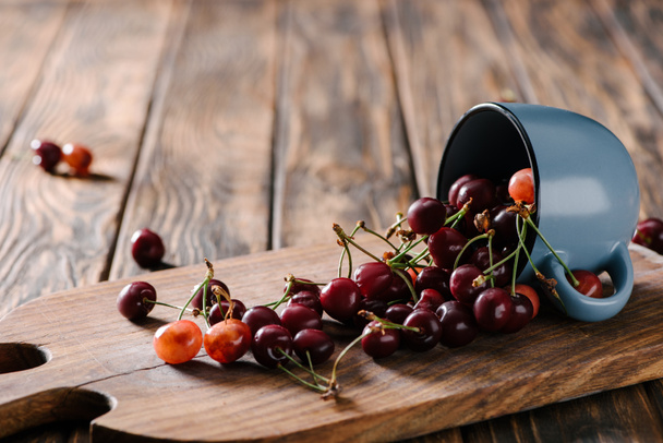 close-up view of organic sweet cherries in blue cup on wooden cutting board on table     - Fotografie, Obrázek