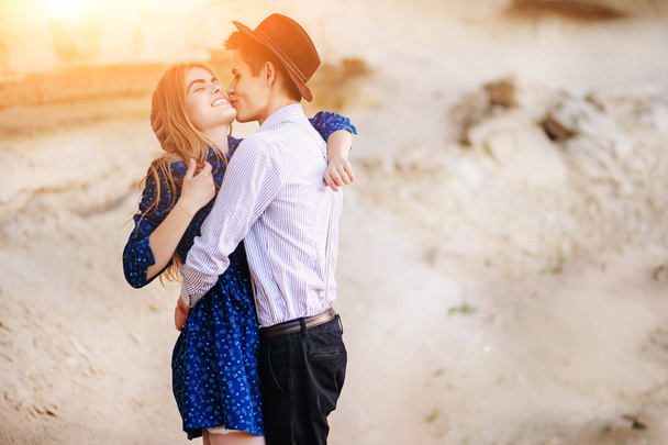 Привлекательный мужчина обнимает и целует красивую женщину в синем платье посреди песчаного каньона
. - Фото, изображение