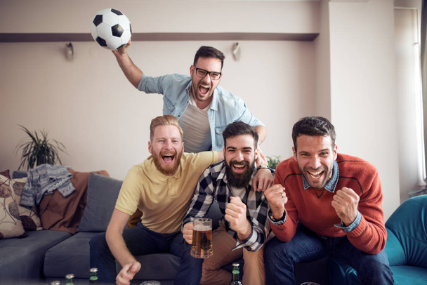 Futbolistas emocionalmente viendo el juego en la sala de estar con cerveza
. - Foto, Imagen