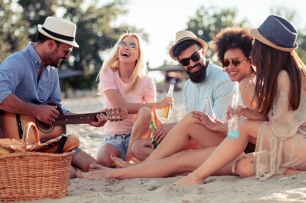fröhliche junge Leute mit Gitarre, die Spaß am Strand.Sommer, Menschen, Freundschaft, Spaß und Urlaubskonzept. - Foto, Bild