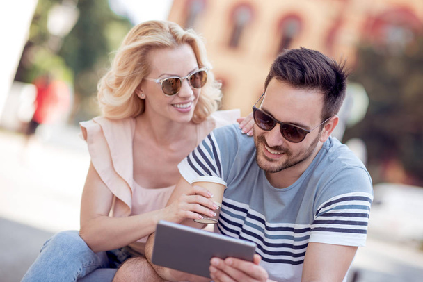 Man and woman drinking coffee and sitting in city park in summer and using tablet computer. - Photo, Image