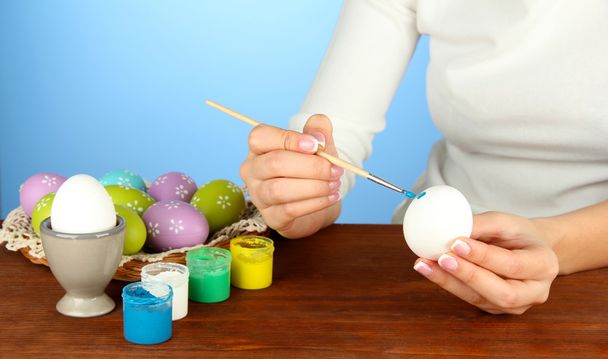 Young woman painting Easter eggs, on color background - Fotó, kép