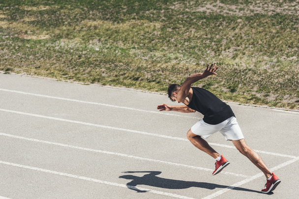 young male sprinter taking off from starting position on running track - Photo, Image