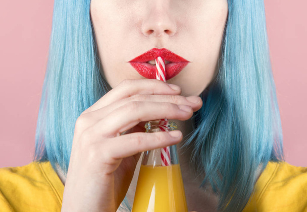 Vértes stúdió portré csípő fiatal nő a vörös rúzs, és kék festett haj iszik narancslé retro üveg szalmával. Vértes-ivott a koktél nyári női száj. Trendi pasztell színű háttér.  - Fotó, kép