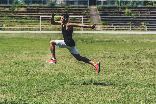 visão lateral do jovem desportista pulando no campo de jogos
  - Foto, Imagem