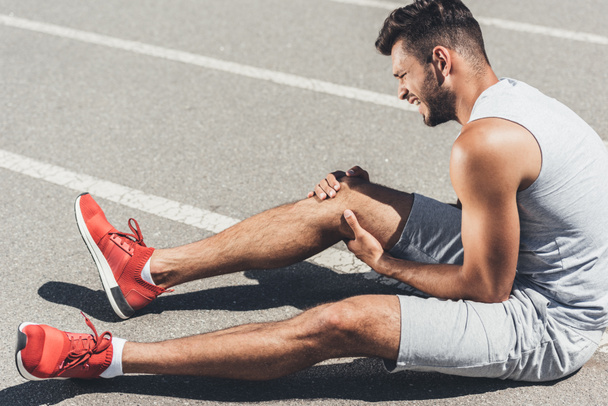 atletico giovane corridore con infortunio alla gamba seduto sul pavimento della pista da corsa
 - Foto, immagini