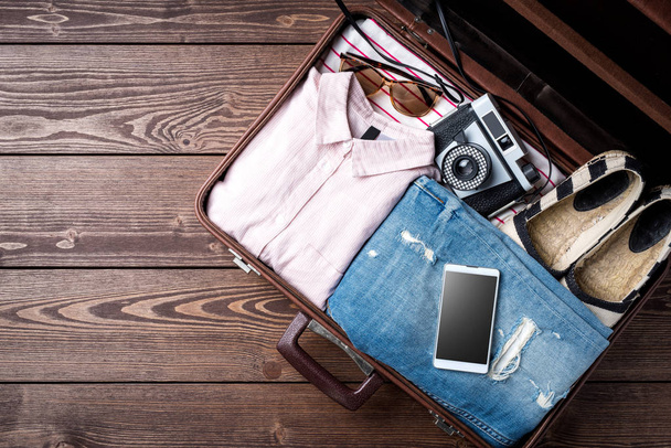 Open suitcase with casual female clothes on wooden table - Foto, Bild