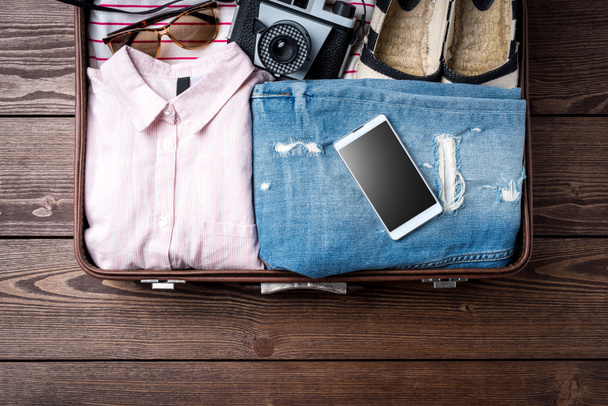 Open suitcase with casual female clothes on wooden table - Photo, Image