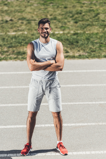 smiling sporty young man with crossed arms looking at camera on running track - 写真・画像
