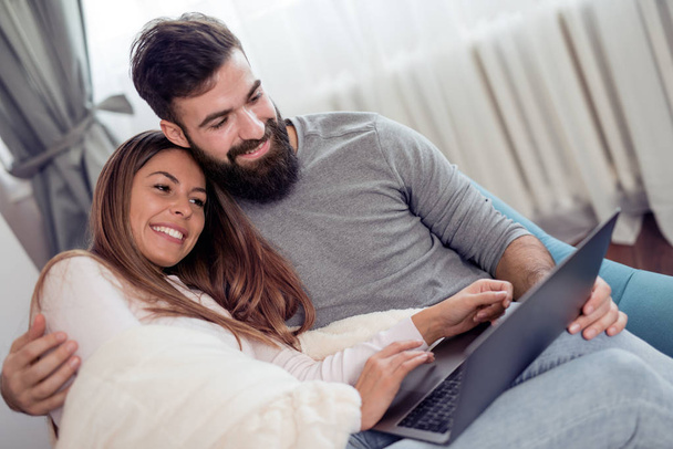 junges Paar sitzt im Wohnzimmer und nutzt Laptop, um online etwas einzukaufen. - Foto, Bild