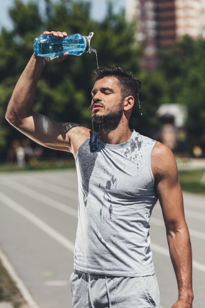 athletic young man pouring water on himself after training - Photo, Image