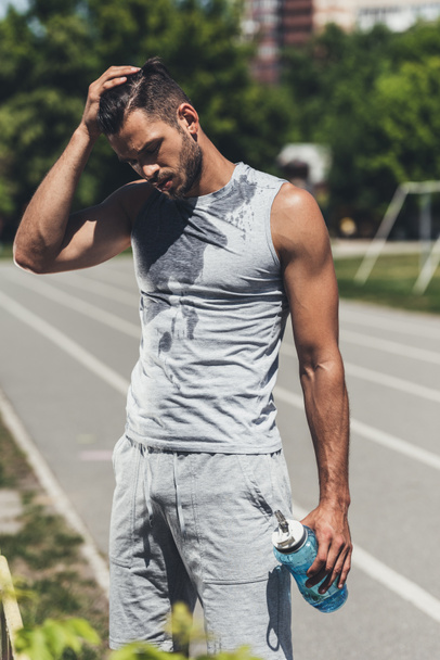 knappe jongeman in natte shirt met fitness fles op de atletiekbaan - Foto, afbeelding