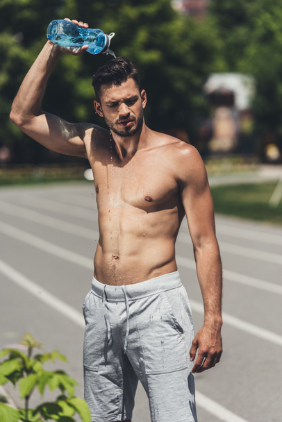 handsome shirtless young man pouring water on himself after training - Фото, зображення