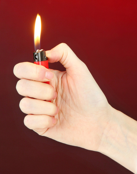 Burning lighter in female hand, on dark red background - 写真・画像