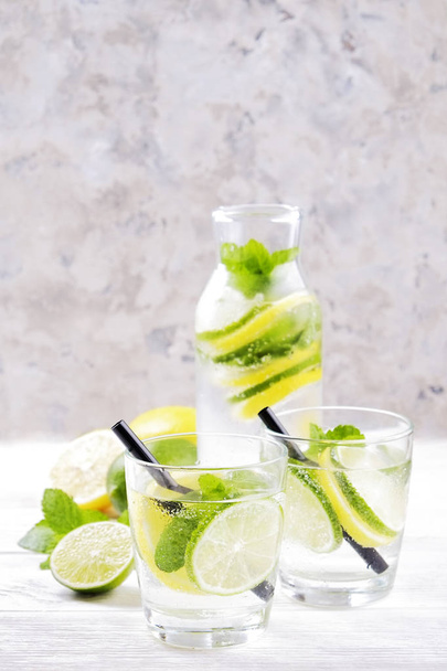 Vintage bottle with two glasses of refreshing non alcoholic mojito lemonade drink with lemon, lime slices, mint leaves, straw, ice on wooden table, concrete background. Close up, top view, copy space. - Foto, Imagem