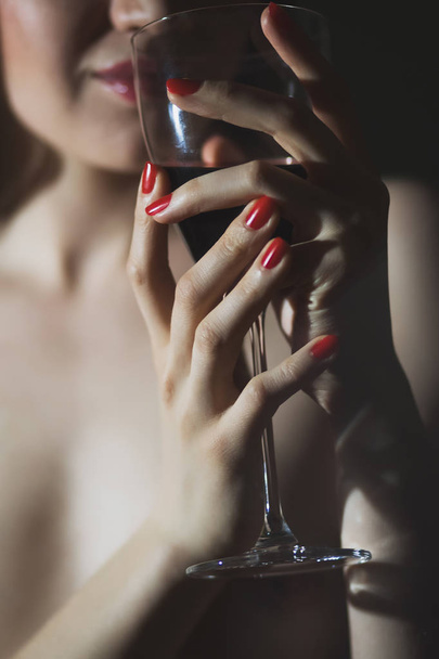 Crop shot of naked woman in tights covering intimate place with wineglass standing in neon light - Foto, Imagem