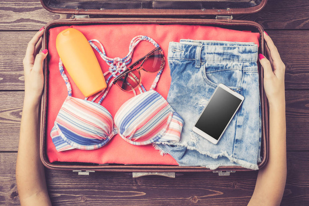 Open suitcase with summer or beach clothes and accessories on wooden table - Foto, Bild