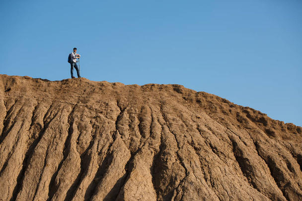 Photo of afar of tourist man with sticks for walking on hill against blue sky - Fotografie, Obrázek