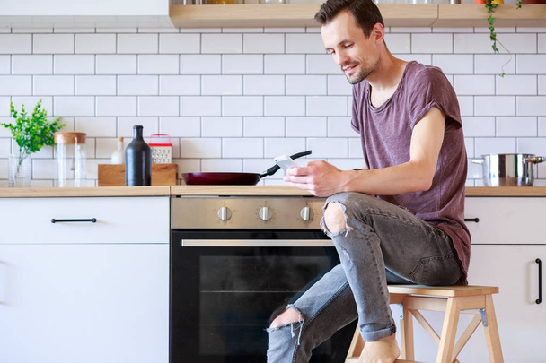 Image of man with frying pan and phone in hands in kitchen at apartment - Fotoğraf, Görsel