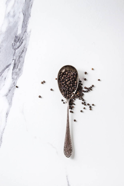 Black pepper peppercorns in vintage spoon over white marble texture background. Top view, space. - Fotoğraf, Görsel