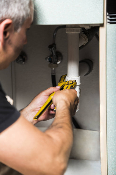 specialist male plumber repairs faucet in kitchen - Valokuva, kuva