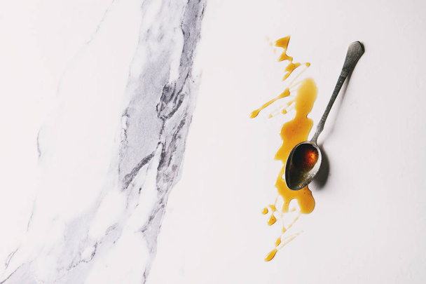 Zelfgemaakte vloeibare transparant bruine suiker karamel in vintage lepel over witte marmeren achtergrond. Platte lay, ruimte. - Foto, afbeelding