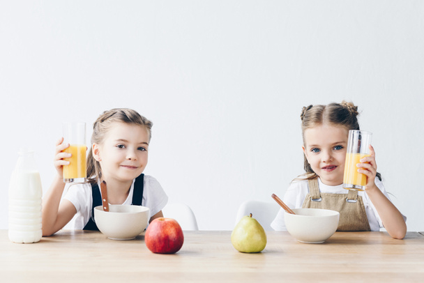Lächelnde Schulmädchen mit Müsli und Gläsern Orangensaft zum Frühstück - Foto, Bild