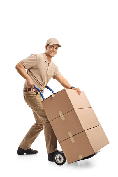 Delivery man with a hand truck loaded with boxes looking at the camera and smiling isolated on white background - Foto, Imagem