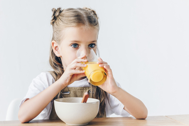 little schoolgirl drinking orange juice during breakfast isolated on white - Photo, Image
