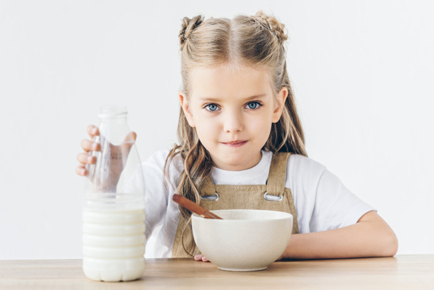 cute little schoolgirl with bowl of cereal and bottle of milk isolated on white - Photo, Image