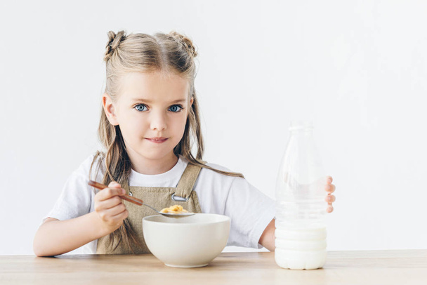 adorable little schoolgirl eating cereal with milk for breakfast isolated on white - Foto, Imagem