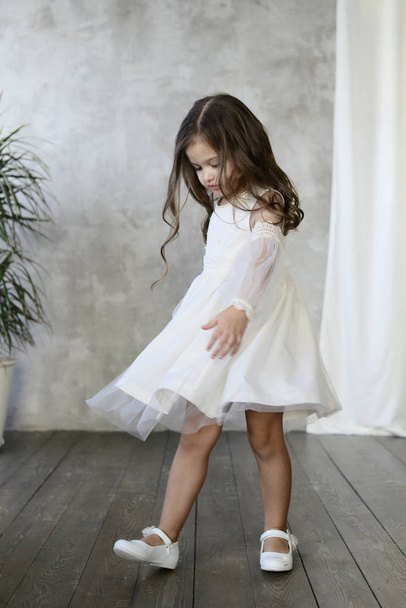 fashionable brunette girl wearing white dress posing on grey wall background, Children lookbook concept  - Fotografie, Obrázek