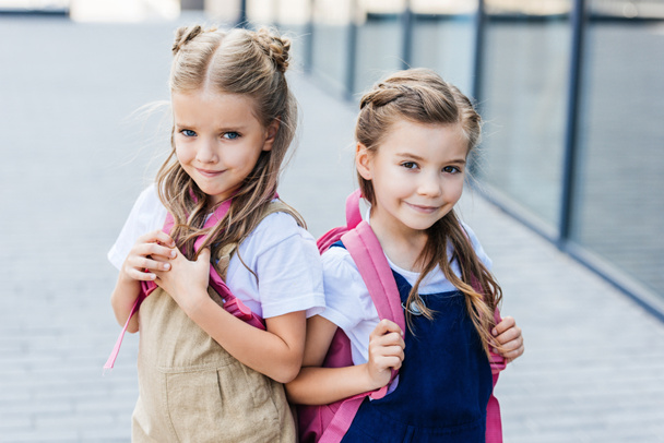 smiling little schoolgirls with pink backpacks on street looking at camera - 写真・画像