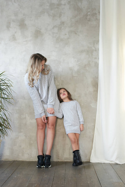 Mom and daughter in wearing same grey pullovers having fun at photo shoot in studio, lookbook concept - Фото, изображение