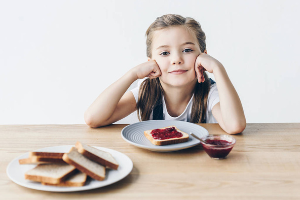 smiling little schoolgirl with toasts and jam for breakfast looking at camera isolated on white - 写真・画像