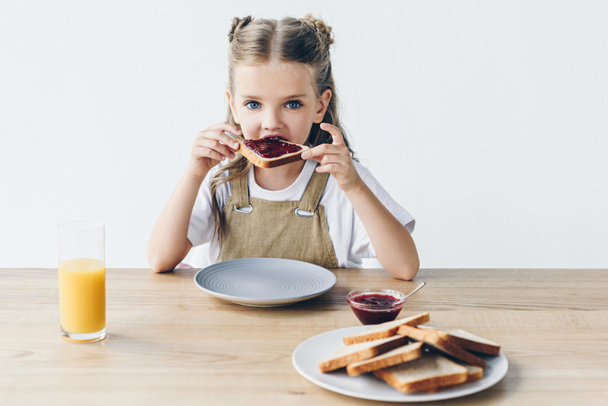 adorable little schoolgirl eating toast with jam isolated on white - Photo, Image