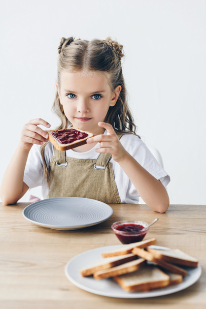 beautiful little schoolgirl eating toast with jam isolated on white - Photo, Image