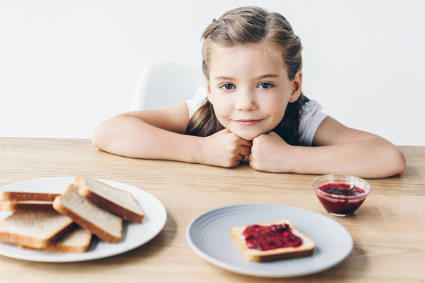 adorable little schoolgirl with toasts and jam for breakfast looking at camera isolated on white - 写真・画像