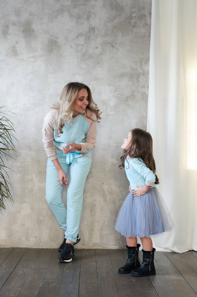 Mom and daughter in same clothes having fun at photo shoot in studio, lookbook concept  - Фото, изображение