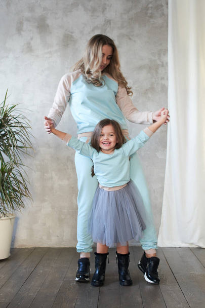 Mom and daughter in same clothes holding hands while posing in studio, lookbook concept  - Foto, Bild