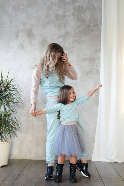 Mom and daughter in same clothes holding hands while posing in studio, lookbook concept   - Fotoğraf, Görsel