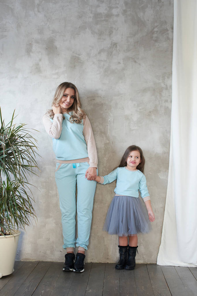 Mom and daughter in same clothes holding hands while posing in studio, lookbook concept   - Foto, imagen